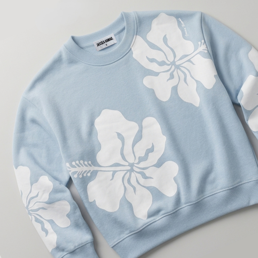 A light blue crewneck sweatshirt with large white hibiscus floral prints on the front and sleeves, shown on a neutral light gray background.